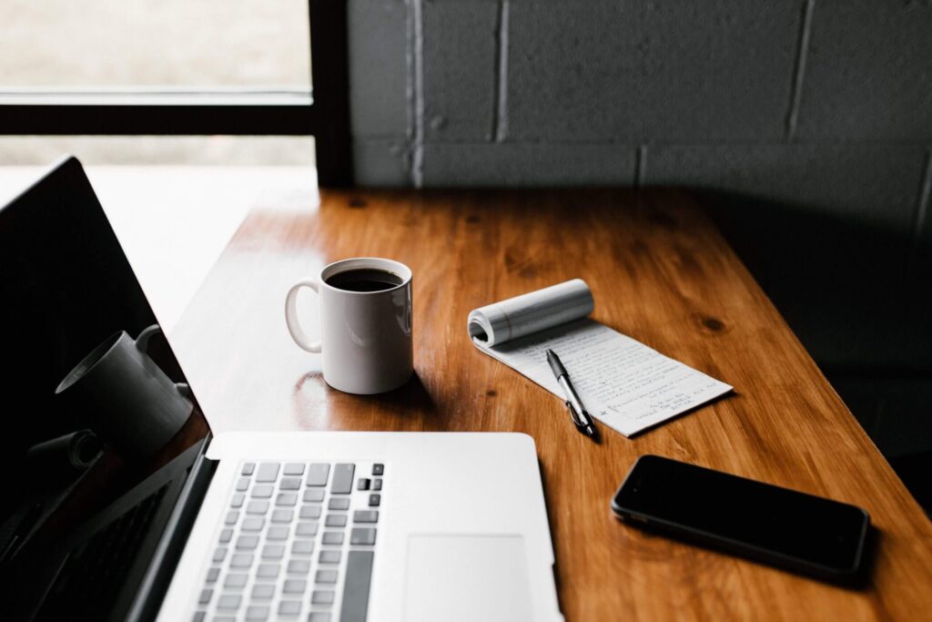 MacBook Pro, white ceramic mug,and black smartphone on table, handling technology safely