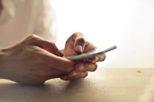 A close-up shot of a woman holding a phone, with her hands, phone and shirt visible.